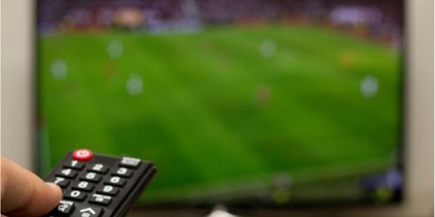 World Cup Football and Domestic Abuse Awareness – Legal Support in Lancashire Hand holding a TV remote while watching a blurred football match, illustrating rising domestic abuse reports during World Cup events and the need for legal support in Lancashire.