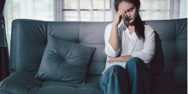 Woman sitting on a sofa looking distressed, representing concerns about being left out of a Will on the Fylde Coast