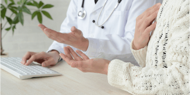 Doctor Consulting Patient During Medical Appointment Doctor in consultation with a patient, discussing medical concerns at a desk with a keyboard and stethoscope visible.