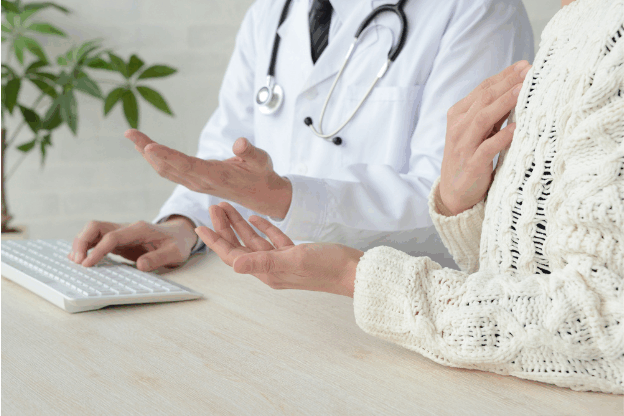Doctor in consultation with a patient, discussing medical concerns at a desk with a keyboard and stethoscope visible.