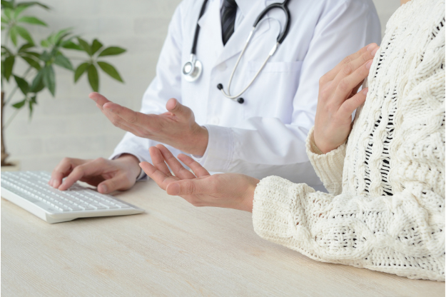 Doctor in consultation with a patient, discussing medical concerns at a desk with a keyboard and stethoscope visible.