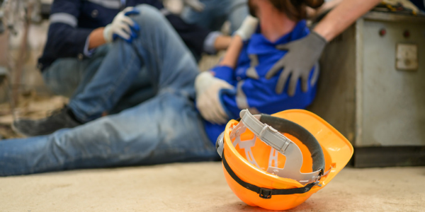 Accident at work claim Orange hard hat on a factory floor as colleagues help an injured worker, the start of an accident at work claim.