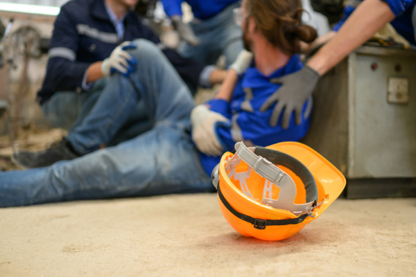 Orange hard hat on a factory floor as colleagues help an injured worker, the start of an accident at work claim.